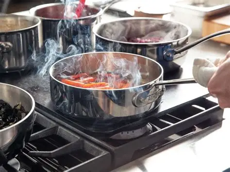 A person holds a saucepan over a stove, with vegetables inside emitting steam or smoke. Other pots are visible in the background.