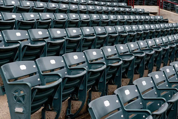 Rows of empty dark green stadium seats with metal armrests and numbered plaques, viewed at an angle.