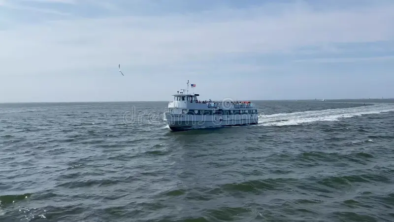 A white passenger ferry travels across a calm, open sea under a partly cloudy sky, leaving a visible wake behind.